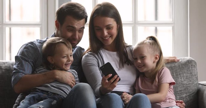 Cheerful parents and kids laughing using funny app on cellphone