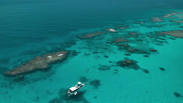 Boat at diving location with coral and pristine blue waters by drone