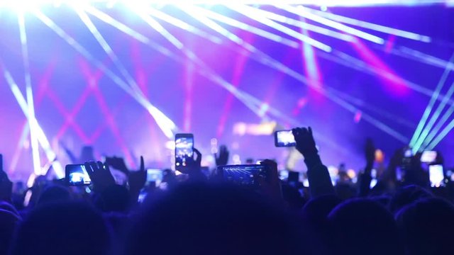 Singer thanks and bows to the fans on stage, blurred background.Phones in the hands of a crowd of viewers take videos and photos at a music festival. Concert live streaming mobile phone hand.
