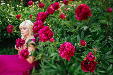 Fototapeta na wymiar Outdoor close up portrait of beautiful young woman with long blonde hair, makeup, posing in the blooming garden. Female spring fashion concept