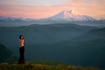 A beautiful young girl with a naked back is standing in an evening dress in the mountains of the...