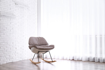 Comfortable rocking chair near white brick wall. Space for text