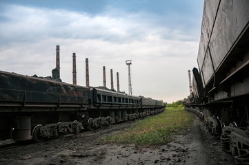train of tipping cars loaded with raw iron ore at wagon unloading platform of ore dressing factory on industrial background