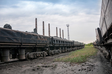 train of tipping cars loaded with raw iron ore at wagon unloading platform of ore dressing factory on industrial background