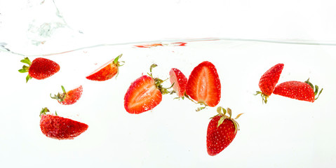 pieces of strawberries falling in water, splashes on white background, close-up