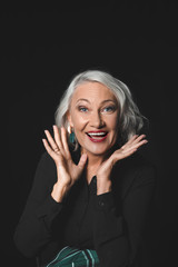 Portrait of stylish excited mature woman on dark background