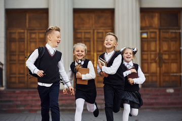 Group of kids in school uniform that is running outdoors together - obrazy, fototapety, plakaty
