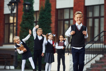 Group of kids in school uniform posing to the camera outdoors together near education building