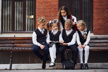 School kids in uniform that sits outdoors on the bench with notepad