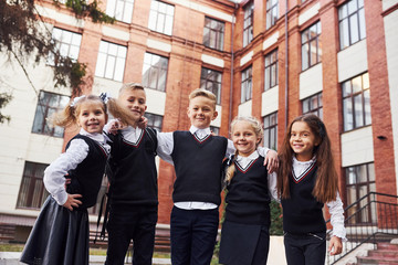 Having fun and embracing each other. Group of kids in school uniform that is outdoors together near...