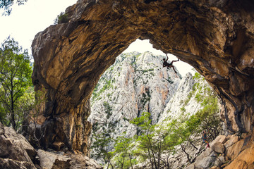 Rock climber climbs on a rock in the form of an arch.