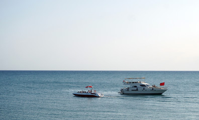 A white luxury motor boat and a pleasure boat sail on the sea in different directions, resting passengers greet each other and wave their hands. Enjoy your holiday at sea while relaxing at the resort.