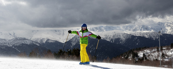 Happy young skier with ski poles in sun mountains and cloudy gray sky before blizzard