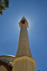 Obraz premium A mosque's minaret captured. The sunshine is coming from behind the minaret. There is a Turkish flag over the minaret.
