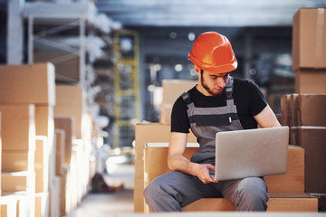 Storage worker in uniform and modern laptop in hands checks production