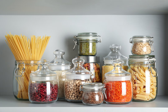 Glass jars with different types of groats and pasta on white shelf