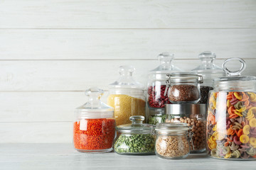 Glass jars with different types of groats and pasta on white wooden table