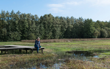 Naklejka na ściany i meble mature woman is resting in nature on a wooden platform in the Veluwe