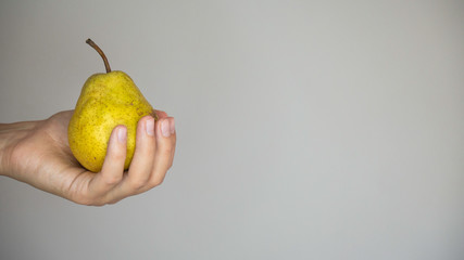Hand of a woman holding yellow pear.