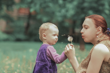 young mother teaches her little daughter to blow on a dandelion