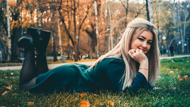 A portrait of a beautiful girl, lying on the grass. A charming woman lies on the green grass with yellow leaves.