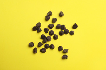 Delicious chocolate chips on yellow background, top view