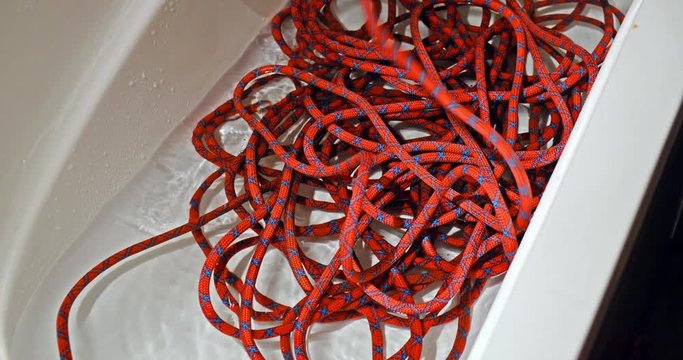 Male hands flaking a climbing rope in a bathtub partially filled with water, then swishing it around. Rope cleaning at home.