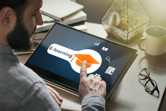 Bearded man with laptop at his desk. He presses on the graduation hat icon. Concept of modern technology in education. Image