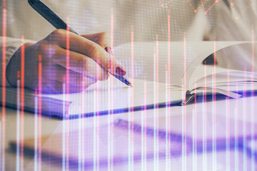 Double exposure of woman's hands making notes with forex graph hologram. Concept stock market analysis.