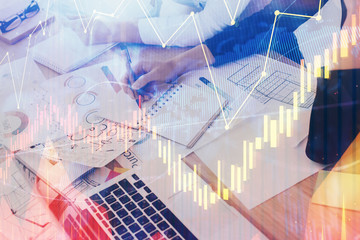 A woman hands writing information about stock market in notepad. Forex chart holograms in front. Concept of research. Double exposure