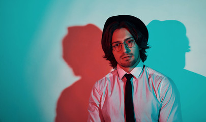 Portrait of young stylish man in hat and with glasses that stands in neon lights in the studio