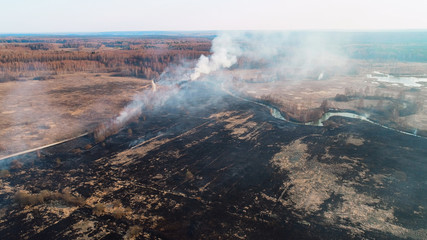 Black burned field, a bush burns in the distance and there is a strong thick smoke. A small river blocks the path of fire.
