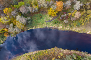 Forest in autumn colors. Colored trees and a meandering blue river. Red, yellow, orange, green deciduous trees in fall. Koiva national park, Latvia, Europe