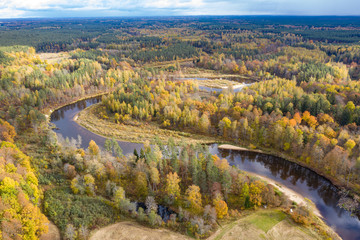 Forest in autumn colors. Colored trees and a meandering blue river. Red, yellow, orange, green deciduous trees in fall. Koiva national park, Latvia, Europe