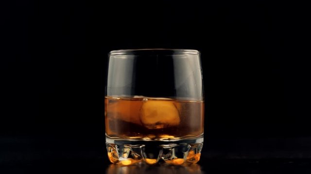 Whiskey Pouring In Glass.Cognac In Glass Floats In Slow Motion.Bourbon Or Rum Pouring In Slow Motion.Running Brandy In Glass From Bottle.Rum Flowing From Brown Bottle.