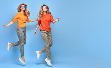 Two Lovable fashionable woman sisters jump in Trendy sunglasses, orange outfit. Studio shot of...