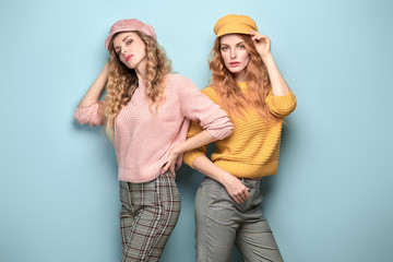 Two easy-going Woman happy smiling in Stylish fashion orange pink colored outfit. Beautiful young Girl in Trendy jumper, cap. Joyful sister, friend, Creative fashionable friendship happiness concept