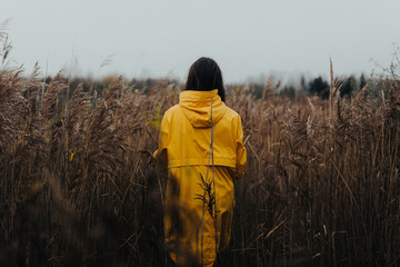 Female in high grass wearing yellow rain coat and looking away from camera - Moody fall scenery with a young girl in bright clothing walking in high grass outdoors