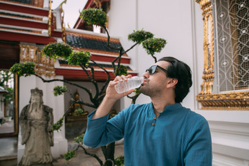 A young man is resting, drinking water in a Buddhist temple.