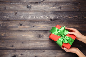 Gift box with ribbon in female hands on wooden background