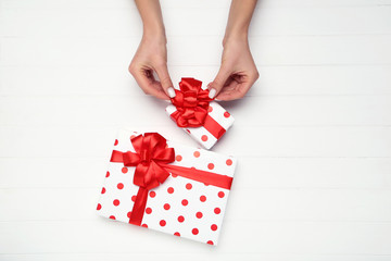 Gift boxes with ribbons and female hands on wooden background