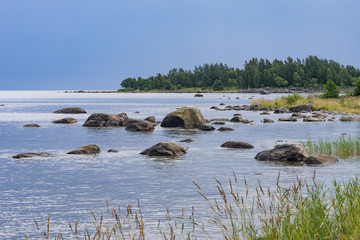 Boulders, forest, shore, evening light, sunset, clouds, blue sky and rainbow on the Baltic Sea. Mohni, small island in Estonia, Europe.
