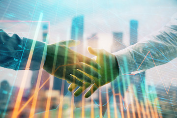 Double exposure of financial graph on cityscape background with two businessman handshake. Concept...