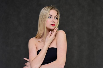 The concept of fashionable glamor, cosmetics and beauty with a pretty girl. Portrait of a fashionable beautiful blonde model with long hair, great makeup, on a gray background.