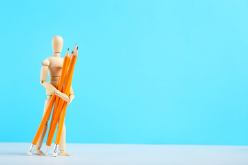 Wooden figure holding pencils on blue background