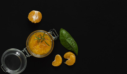 Citrus (tangerine) jam in a glass jar on a black stone table. Flat lay, copy space.