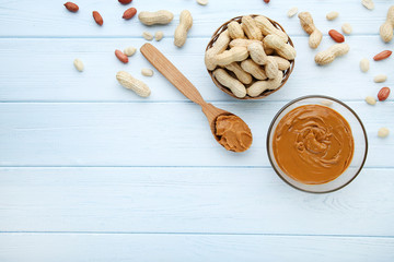 Peanut butter in bowl and nuts on wooden table