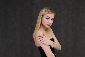 The concept of fashionable glamor, cosmetics and beauty with a pretty girl. Portrait of a fashionable beautiful blonde model with long hair, great makeup, on a gray background.