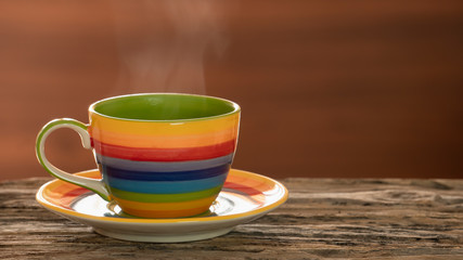 Coffee in multicolour cup, hot coffee with vapour on wooden table and wooden background, selective focus