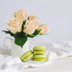 Obraz na płótnie Canvas Two light green French macarons with tender roses in a vase on white background. Close up. Pistachio macarons.